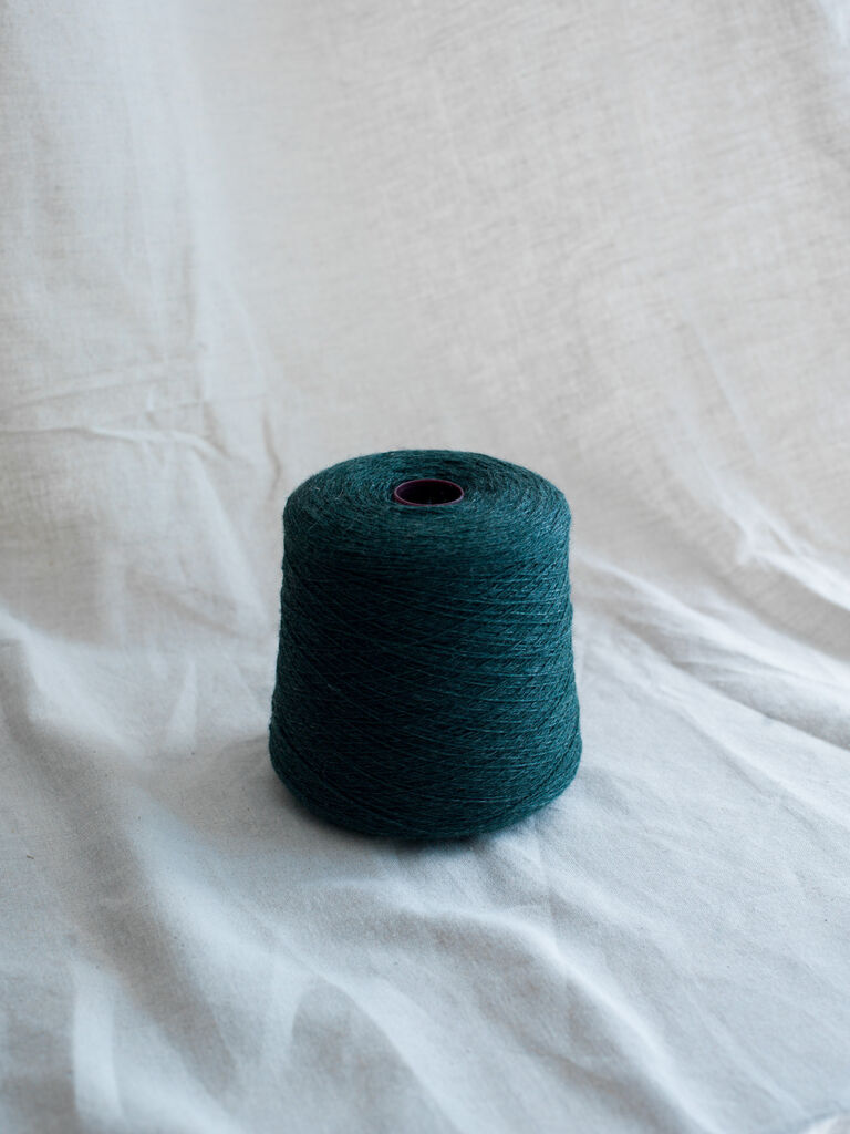 a Cone of dark green yarn centered on a white fabric background