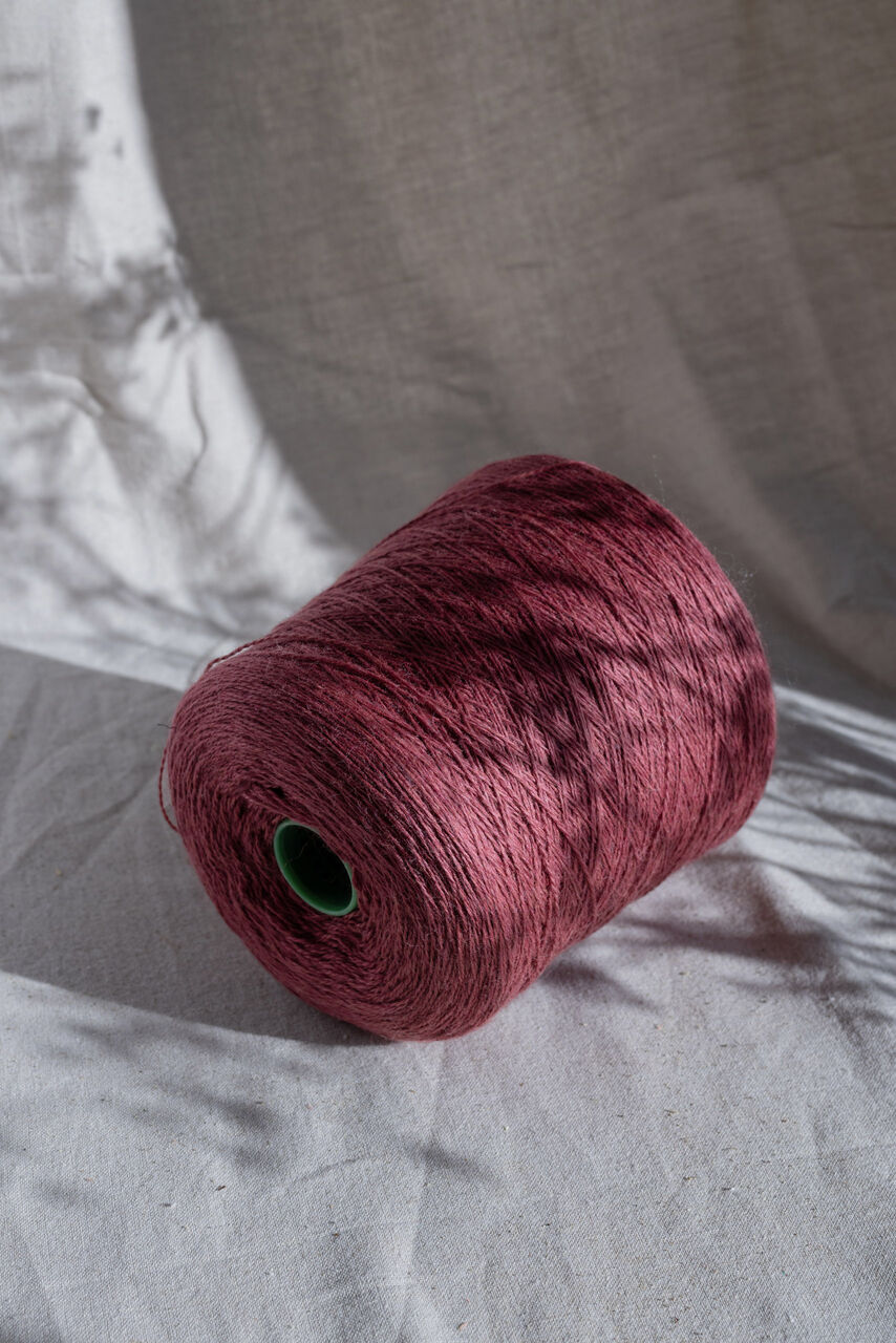 Dark pink cone of yarn on a half shaded linen surface
