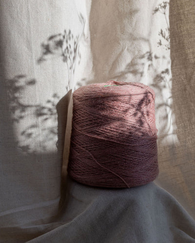 A cone of softened pink yarn on a linen background with blurred floral shadows