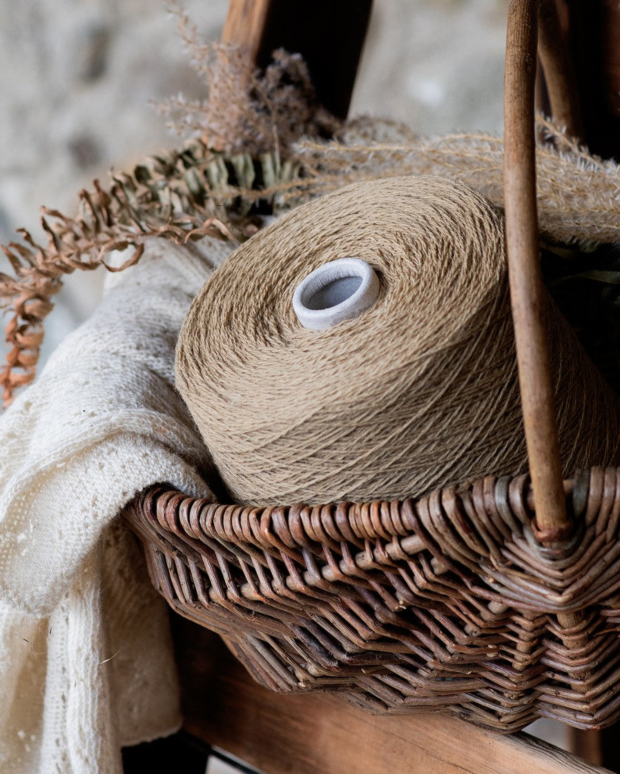 A large light brown-colored wool yarn cone resting on a wicker basket and brown fern leaf decoration.