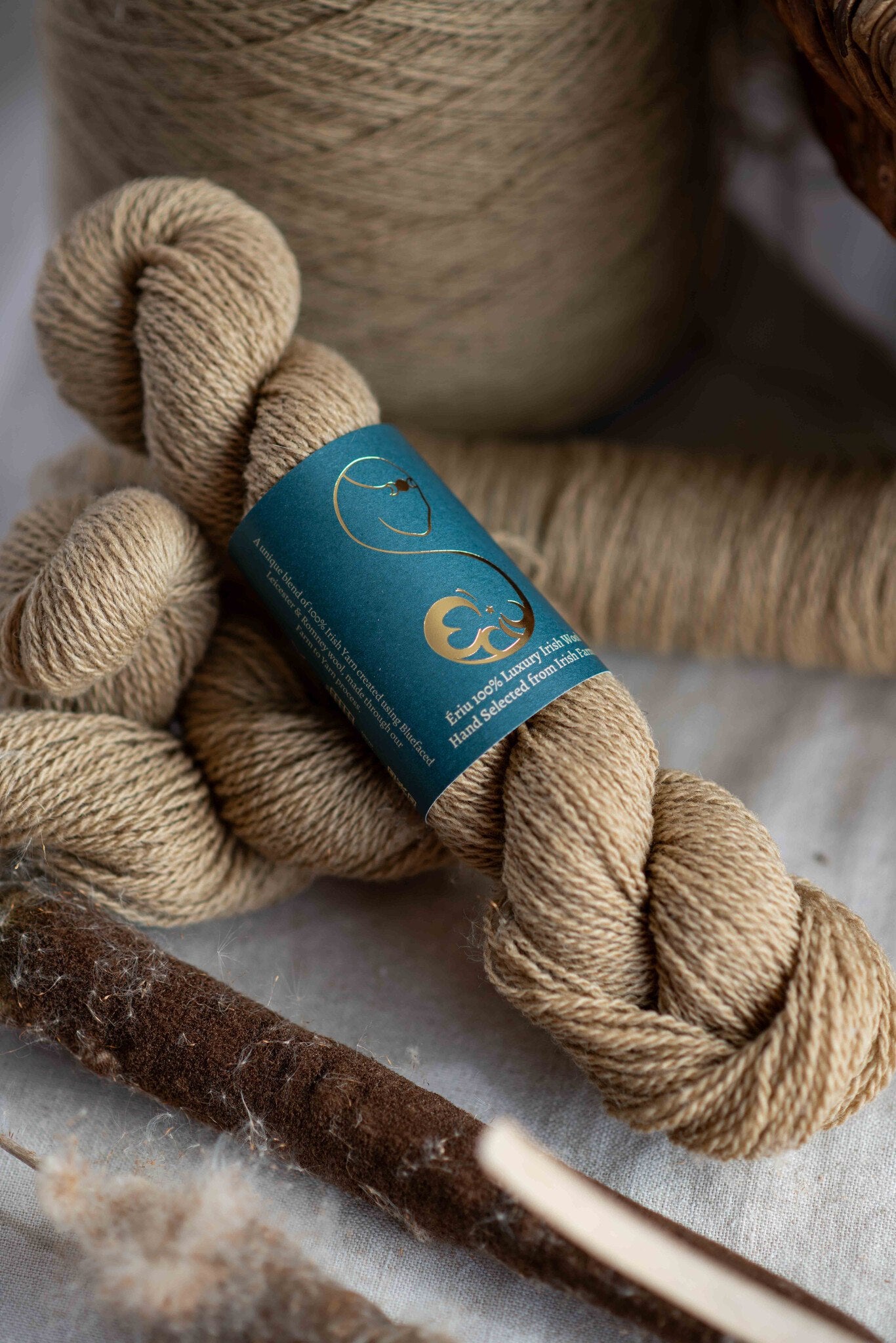 A light brown skein of yarn with a label, beside a reed cattail and a cone of the same light brown wool