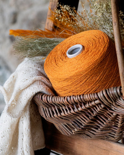 a bright orange cone of wool in a wicker basket with neutral-colored and orange floral decoration