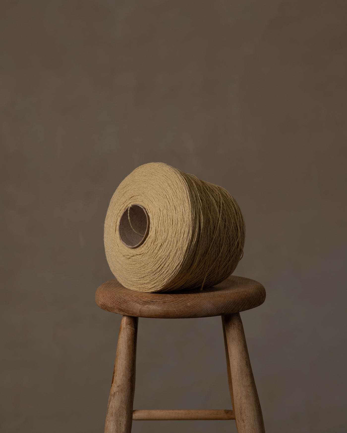 A large golden-colored wool yarn cone placed on a wooden stool against a neutral background.