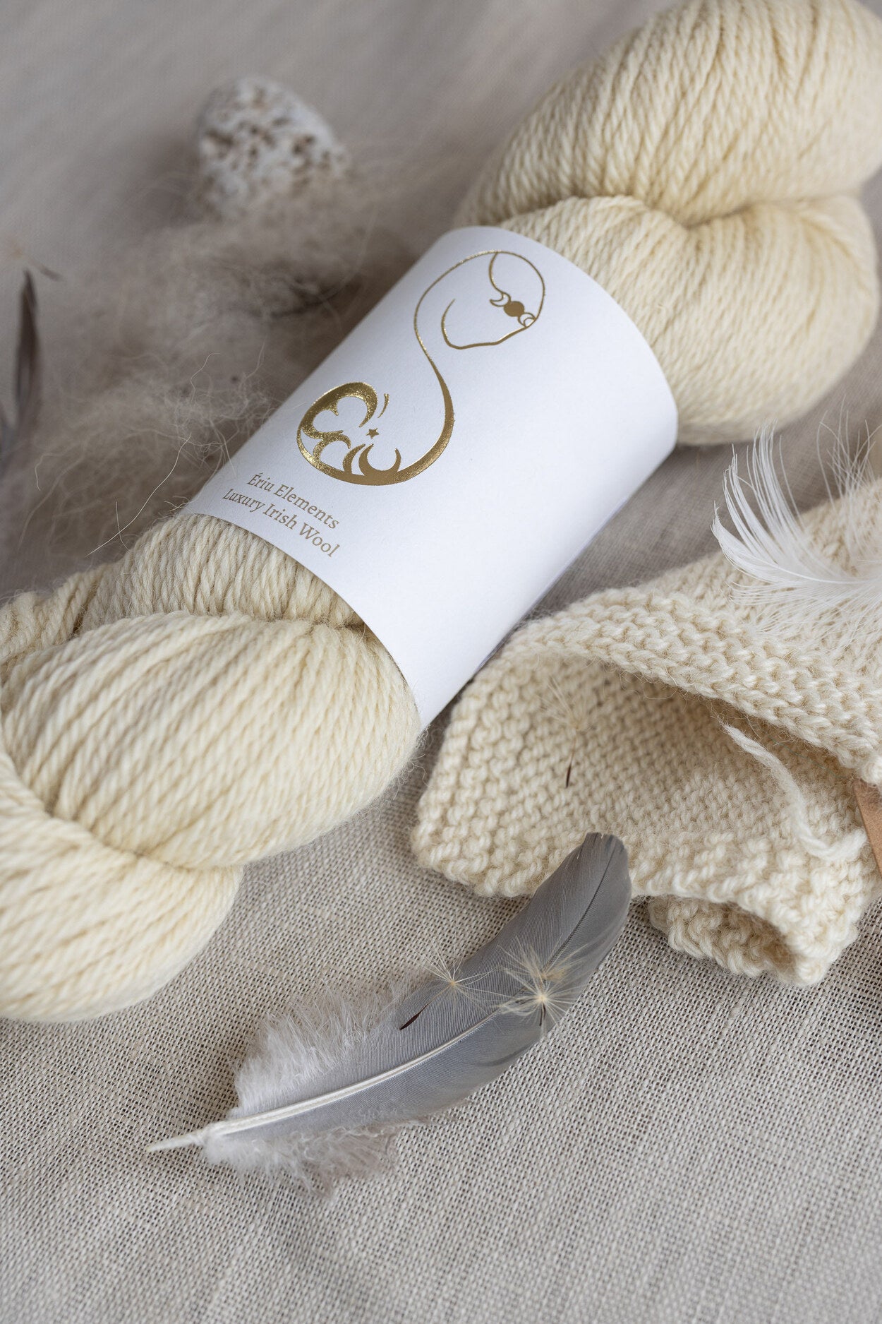 Light cream-colored skein of yarn on white linen accented with down feathers