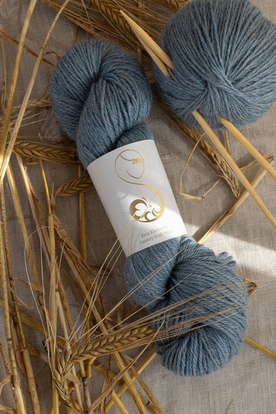 Cadet blue skein of yarn on linen decorated with golden wheat stalks.
