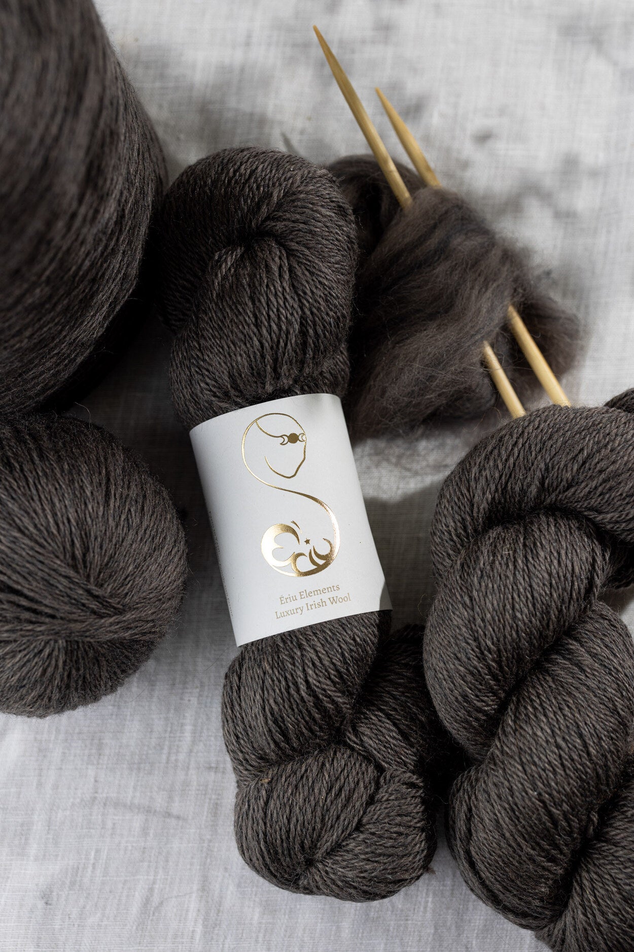 Dark gray yarn skeins with knitting needles on a light gray background