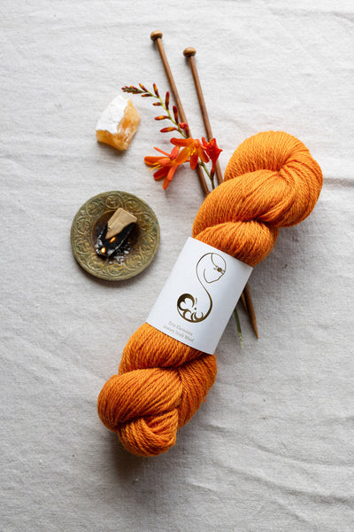 Bright orange skein of yarn with knitting needles and matching amber colored decorative elements on a linen surface