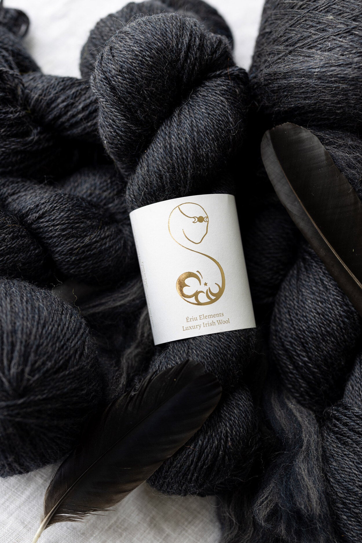 a Deep gray yarn skein decorated with crow feathers and gray yarn on a light background