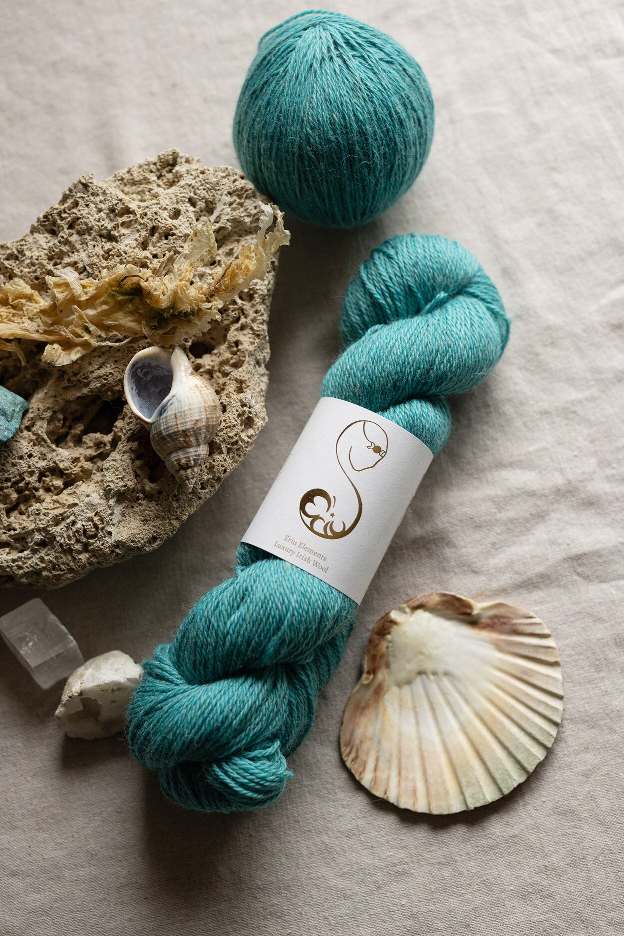 Turquoise luxury Irish wool skeins with a label on a seaside themed surface with shells and coral