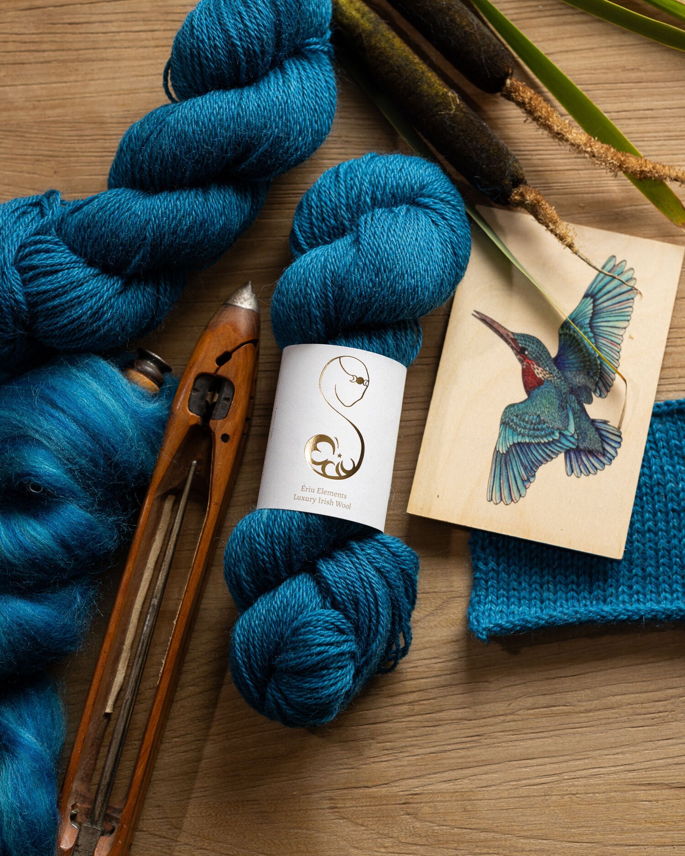 Bright blue yarn skein with knitting needles and a kingfisher illustration on a wooden surface