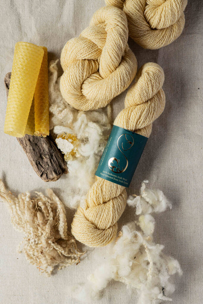 Light yellow skeins of yarn placed on linen decorated with loose wool fibers and a sheet of beeswax
