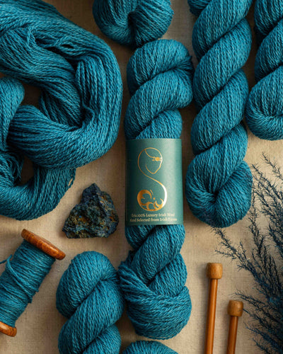 Kingfisher blue labeled wool yarn skeins arranged with knitting needles, a yarn holder and azurite